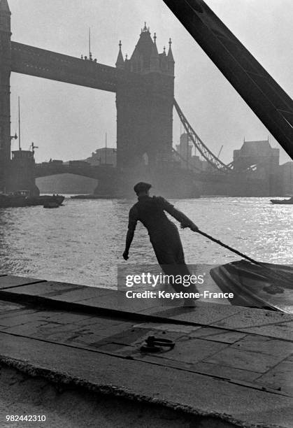 Homme tirant une amarre sur les docks à Londres en Angleterre au Royaume-Uni, en 1936 - En arrière-plan, le Tower Bridge.