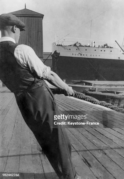 Homme tirant une amarre sur les docks à Londres en Angleterre au Royaume-Uni, en 1936 - En arrière-plan, le navire 'Quebec City'.