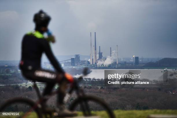 Mountainbiker enjoys the view over the river Rhine to the industrial facilities of ThyssenKrupp in Duisburg, from Halde Rheinpreussen in Moers,...