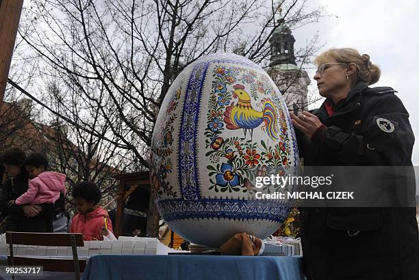 Female worker paints an Easter egg as tourists look at decorated Easter eggs on sales at the traditional Easter market in the Old Town Square in...