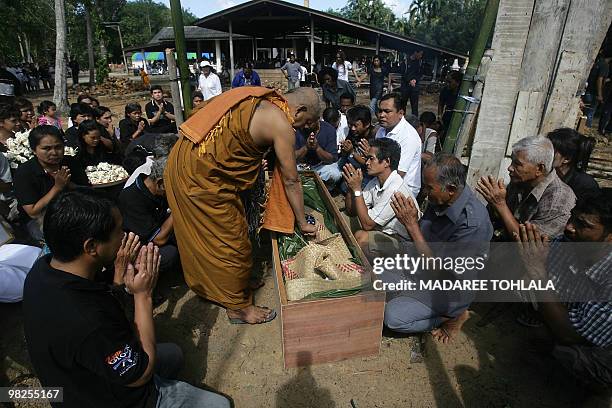 Thai relatives and a Thai Buddhist monk stand next to one of six coffins to be burnt during a funeral procession in Thailand's restive southern...