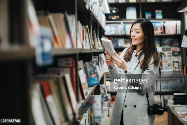 young woman enjoying a quiet time reading book in book store - bookshop stock-fotos und bilder