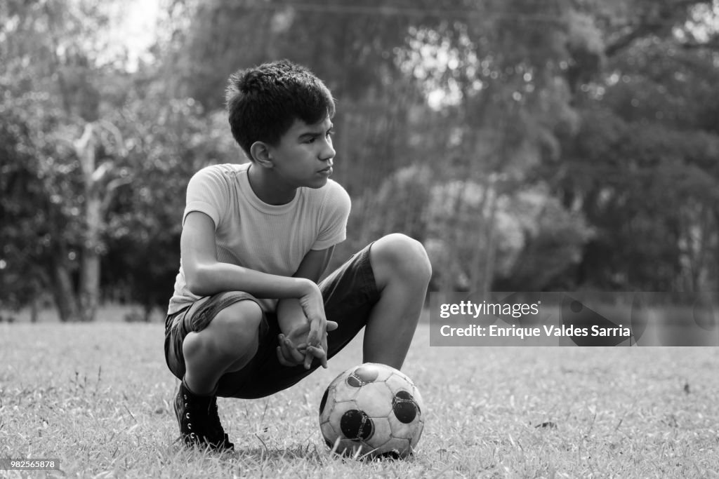 Boy crouching by soccer ball in field, Jamundi, Valle del Cauca, Colombia