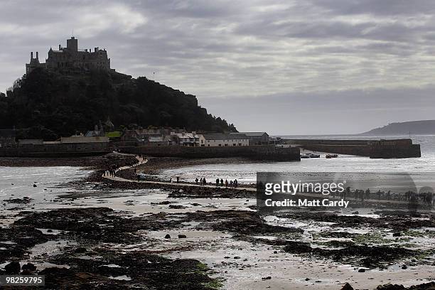 People walk on the beach as kite surfers enjoy the windy weather in Mount's Bay near St Michael's Mount near Penzance on April 5, 2010 in Cornwall,...