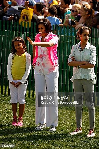 First lady Michelle Obama waves to guests while standing with her daughters Sasha Obama and Malia Obama during the Easter Egg Roll at the White House...