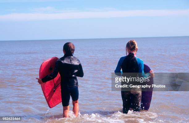 Two children in black wet suits body boarding sea waiting for a wave.