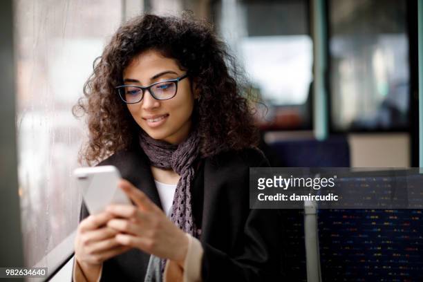 lächelnde junge frau, die mit dem bus unterwegs ist und mit dem smartphone telefoniert. - arab phone stock-fotos und bilder