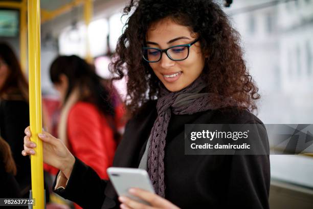 mulher jovem sorridente, viajando de ônibus e usando telefone inteligente - damircudic - fotografias e filmes do acervo