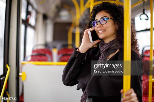 mulher jovem sorridente, viajando de ônibus e usando telefone inteligente - damircudic - fotografias e filmes do acervo