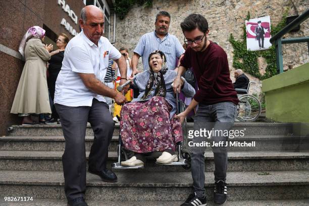 An elderly woman in a wheelchair is helped down some stairs as she leaves Haci Sabanci polling station where he will cast his vote in the Turkish...