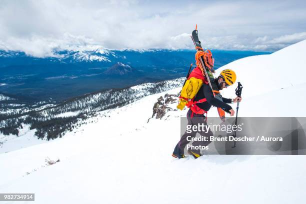 man carrying snowboard up mountain, mt shasta, california, usa - monte shasta foto e immagini stock
