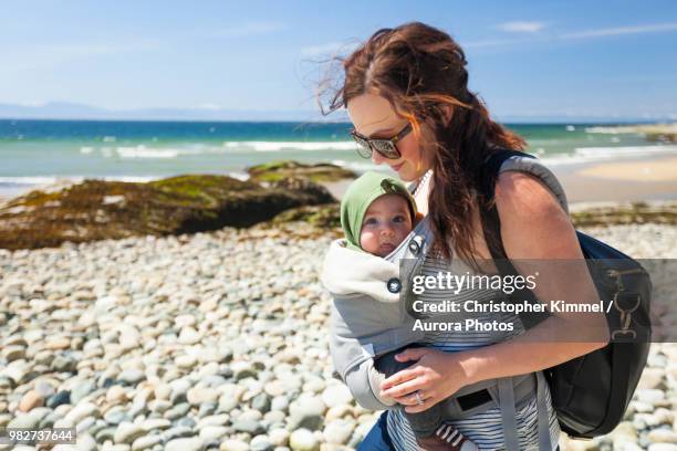 mother with baby son in carrier at beach - babytrage stock-fotos und bilder