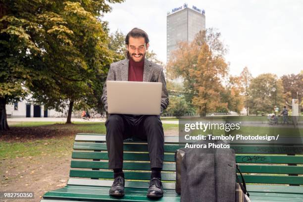 man sitting with laptop on bench in park - parc informatique bureau ordinateur photos et images de collection