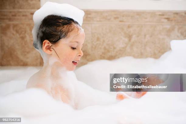 girl sitting in a bubble bath playing with her doll - doll house stockfoto's en -beelden