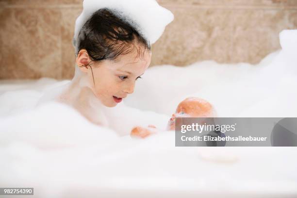 girl sitting in a bubble bath with her doll - doll house stockfoto's en -beelden