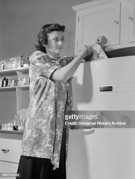 Woman Using Slip of Paper to see if Refrigerator is Wasting Valuable Electric Power and if the Paper can be Pulled out, have the Gasket Tightened or...