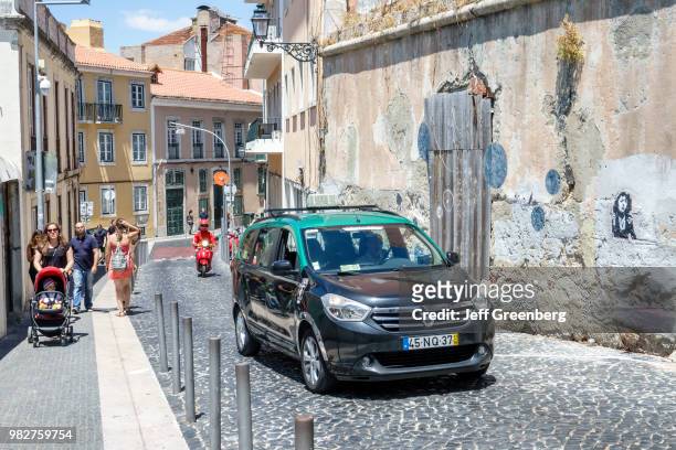 Portugal, Lisbon, Castelo quarter, steep cobblestone street with car and pedestrians.