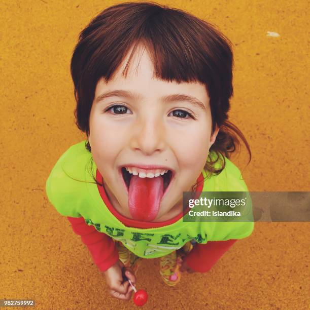 portrait of a smiling girl eating a lollipop and sticking out her red tongue - candy on tongue stock pictures, royalty-free photos & images