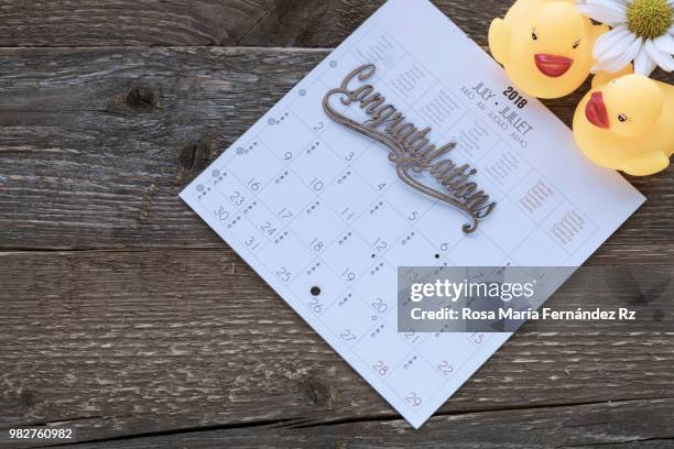 directly above of calendar sheet with work "congratulations", two rubber ducks and white daisy on old wooden background with copy space. - rz stock pictures, royalty-free photos & images