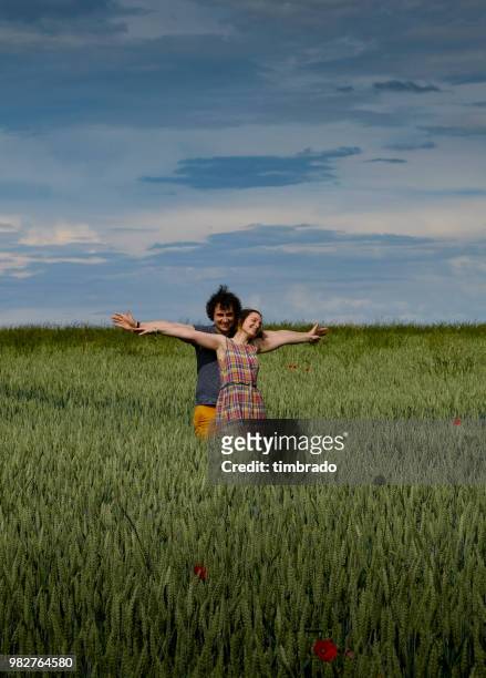 smiling couple standing in a poppy and barley field, niort, nouvelle-aquitaine, france - stehmohn stock-fotos und bilder