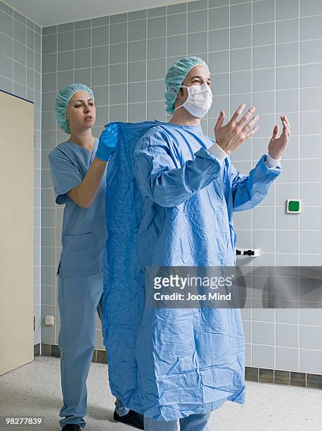 nurse helping surgeon putting on protective clothe - operationskittel stock-fotos und bilder