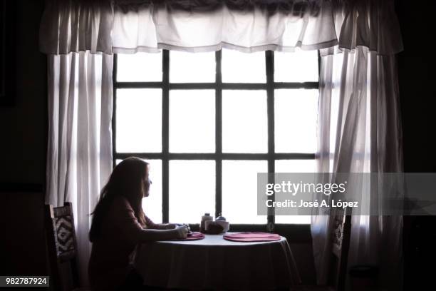 young woman sitting at table in restaurant and looking though window, valle, honduras - view-through-restaurant-window stock pictures, royalty-free photos & images