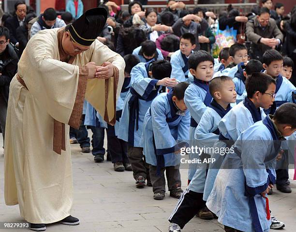Teacher leads a group of young Chinese children dressed in ancient costumes, to pay homage to the statue of Confucius, at the Confucius temple in...