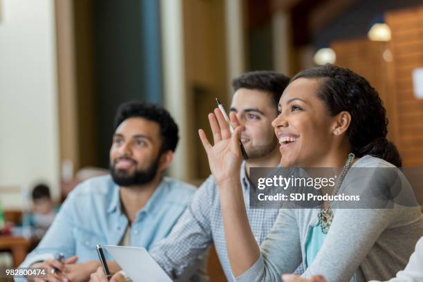 mid adult woman raises hand duirng college class - finding answers stock pictures, royalty-free photos & images