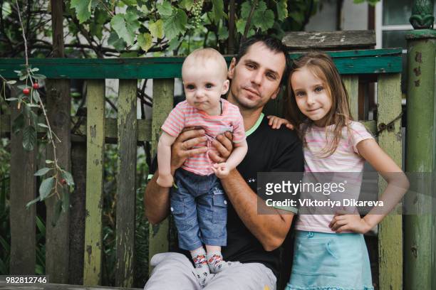 russian family. father with daughter and baby son on a bench near the house. - starving white children fotografías e imágenes de stock