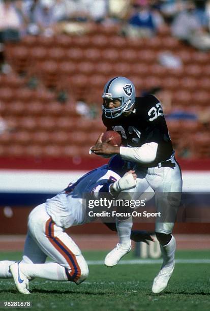 Running Back Marcus Allen of the Los Angeles Raiders tries to run through the tackle of linebacker Randy Gradishar of the Denver Broncos circa mid...