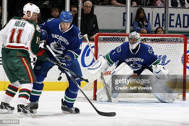 Roberto Luongo of the Vancouver Canucks looks on a Owen Nolan of the Minnesota Wild and Andrew Alberts of the Vancouver Canucks look for a loose puck...