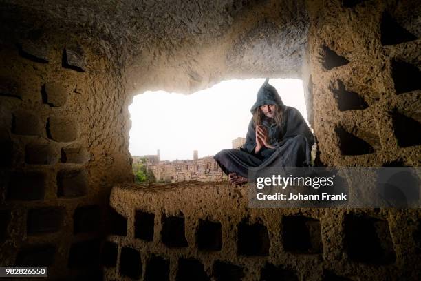 hermit monk in hooded religious habit praying in cave, sorano, tuscany, italy - sotano stock-fotos und bilder