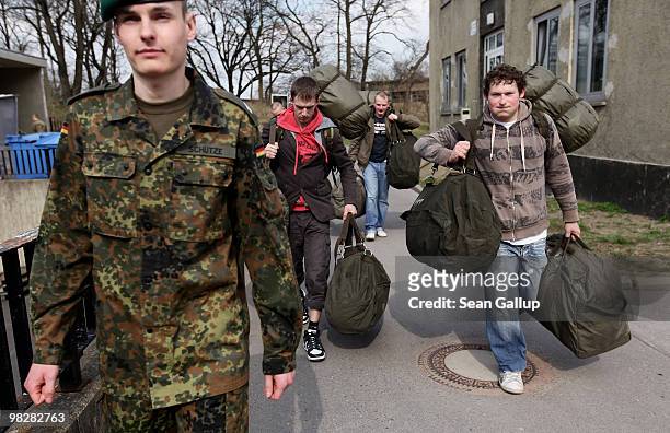Soldier of the German Bundeswehr leads young men lugging bags containing their uniforms and other equipment on their first day of compulsory military...