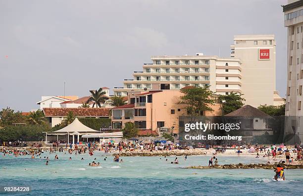 Hotels stand behind tourists on a beach in Cancun, Mexico, on Saturday, April 3, 2010. Passenger traffic at the Cancun airport increased 1.1 percent...