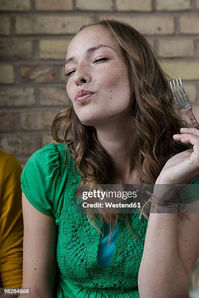 germany, berlin, young woman holding fork, eyes closed, portrait - genuss stock-fotos und bilder