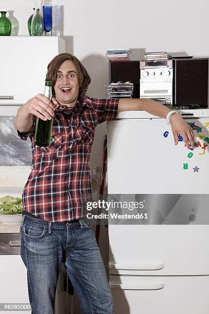 germany, berlin, young man in kitchen holding beer bottle, portrait - beer bottle mouth stock-fotos und bilder