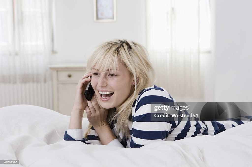 Germany, Berlin, Young woman in bed using cell phone