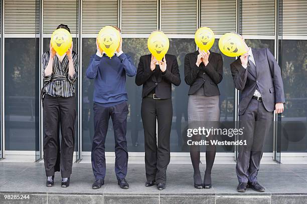 germany, hamburg, five business people standing in front of office building, hiding faces behind balloons - fünf personen stock-fotos und bilder