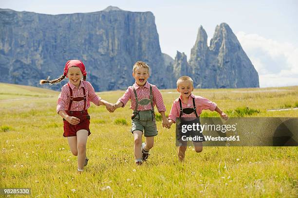 italy, seiseralm, three children (4-5), (6-7), (8-9) running in field - läderbyxor bildbanksfoton och bilder