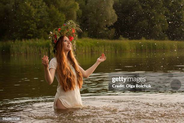 portrait of woman with wreath standing in lake and splashing water - slawische kultur stock-fotos und bilder