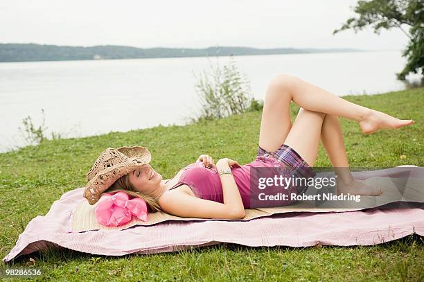 germany, bavaria, starnberger see, young woman lying on blanket in park, smiling, side view, portrait - girl and blond hair and cowboy hat stock pictures, royalty-free photos & images