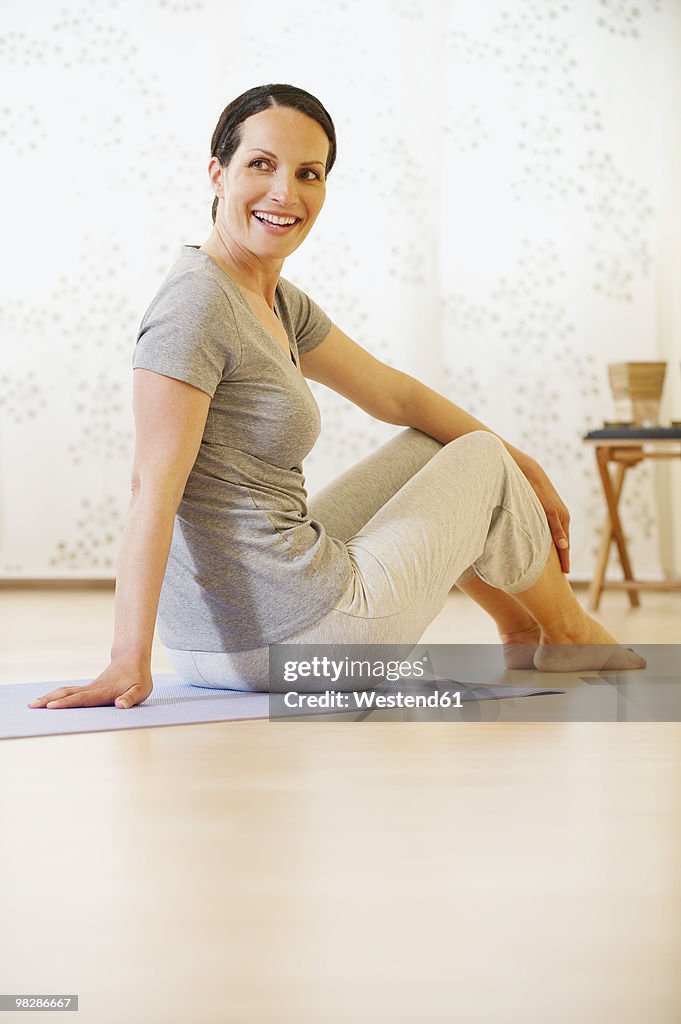 Woman sitting on gym mat, smiling, portrait