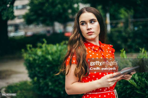 jeune femme en robe rouge dans le parc public, à l’aide de tablette numérique - matrixnis photos et images de collection