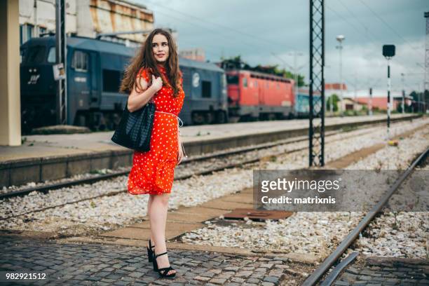 voyageur femme dans une robe rouge se trouve sur la gare ferroviaire - matrixnis photos et images de collection