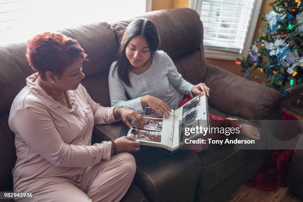 mother and daughter looking at photo album near christmas tree - looking at a photo album stock-fotos und bilder