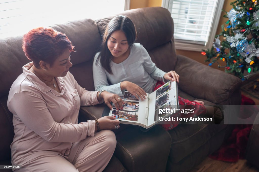 Mother and daughter looking at photo album near Christmas tree