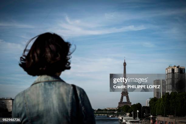 Woman stands on a bridge in front of the Eiffel tower in Paris on June 24, 2018.