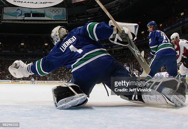 Roberto Luongo of the Vancouver Canucks makes a glove save as his teammate Mason Raymond and Stephane Yelle of the Colorado Avalanche look on during...