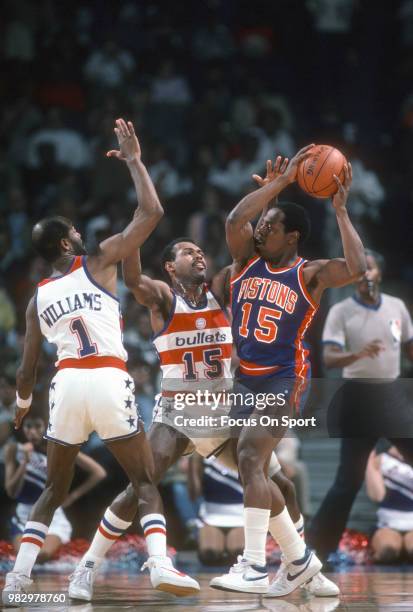 Vinnie Johnson of the Detroit Pistons looks to pass the ball over the top of Frank Johnson and Gus Williams of the Washington Bullets during an NBA...