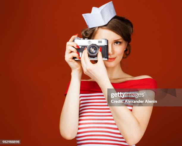 beautiful pin-up girl holding a vintage camera and directs it straight to the camera. red background - pin up girl stockfoto's en -beelden